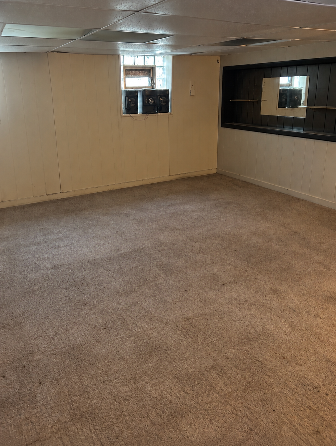 The same basement fully emptied with bare carpet and cleared walls after the cleanout