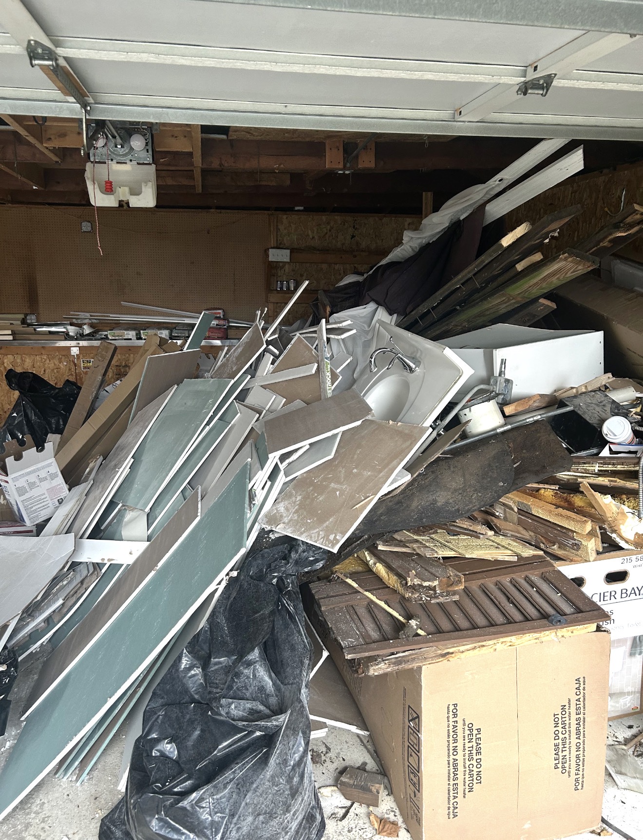 Garage packed with renovation debris, cabinets, drywall and fixtures before the cleanout